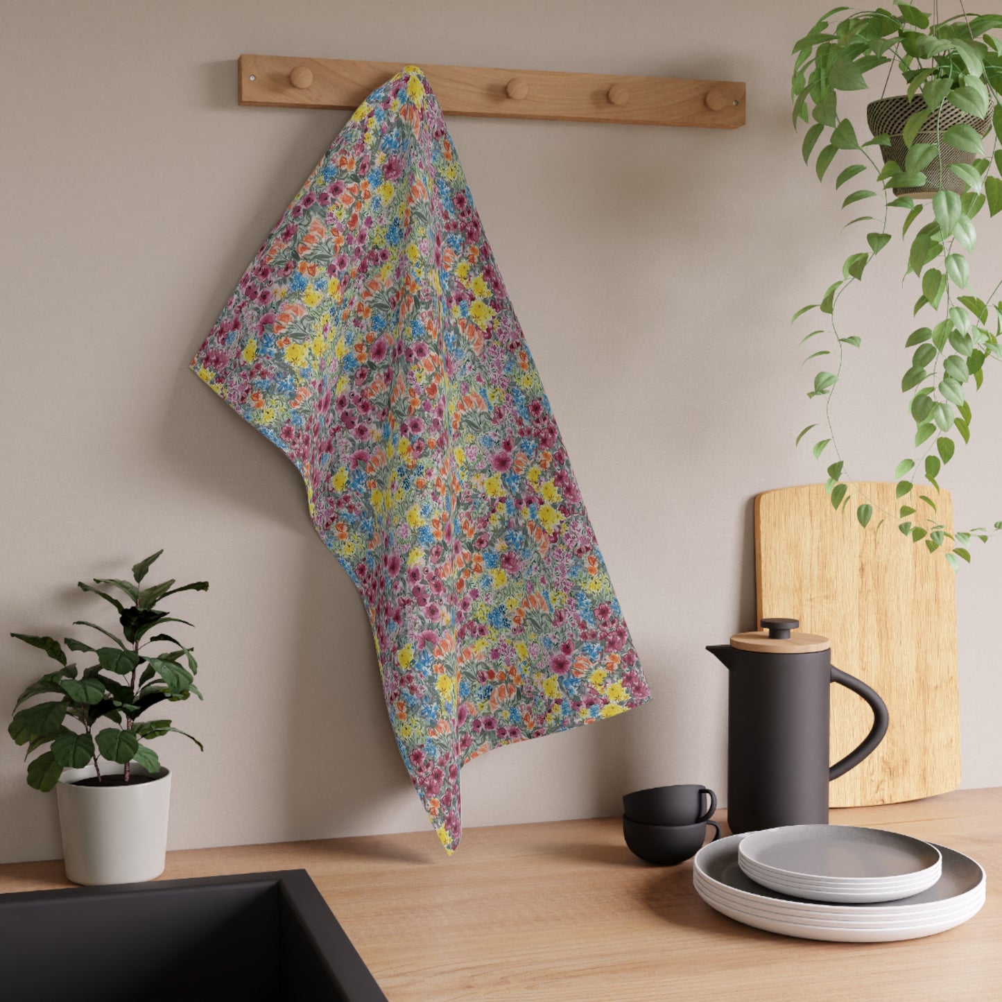 Floral towel hanging on a wooden rack above a kitchen counter with plates, cups, and a plant.