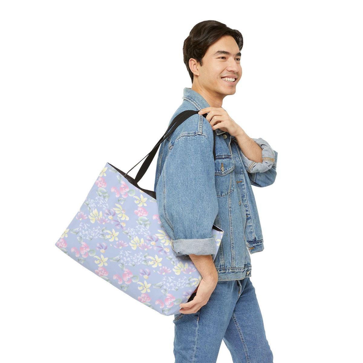 A large tote bag with a floral pattern in pastel colors of pink, yellow, and purple on a light blue background. The bag has black straps and is carried over the shoulder.