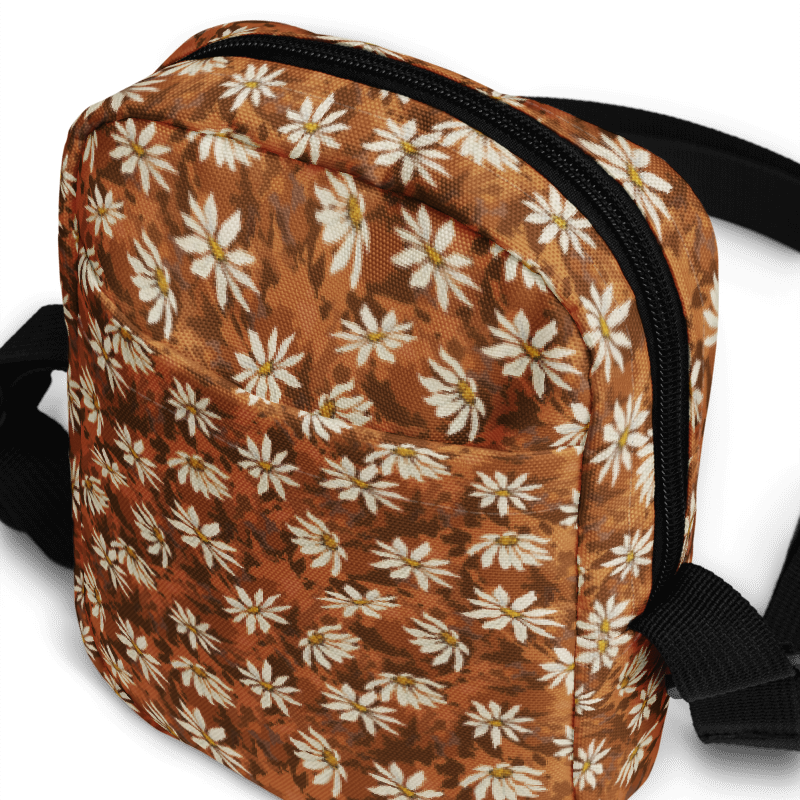Daisy-scatter on textured warm browns bag with a black strap on a white background