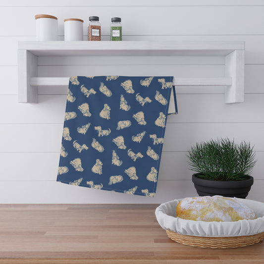 Navy blue kitchen tea towel featuring a repeating hand-drawn dog pattern in soft cream tones, displayed hanging in a bright kitchen with a wooden countertop, herbs, and fresh bread for cozy pet lover home décor.