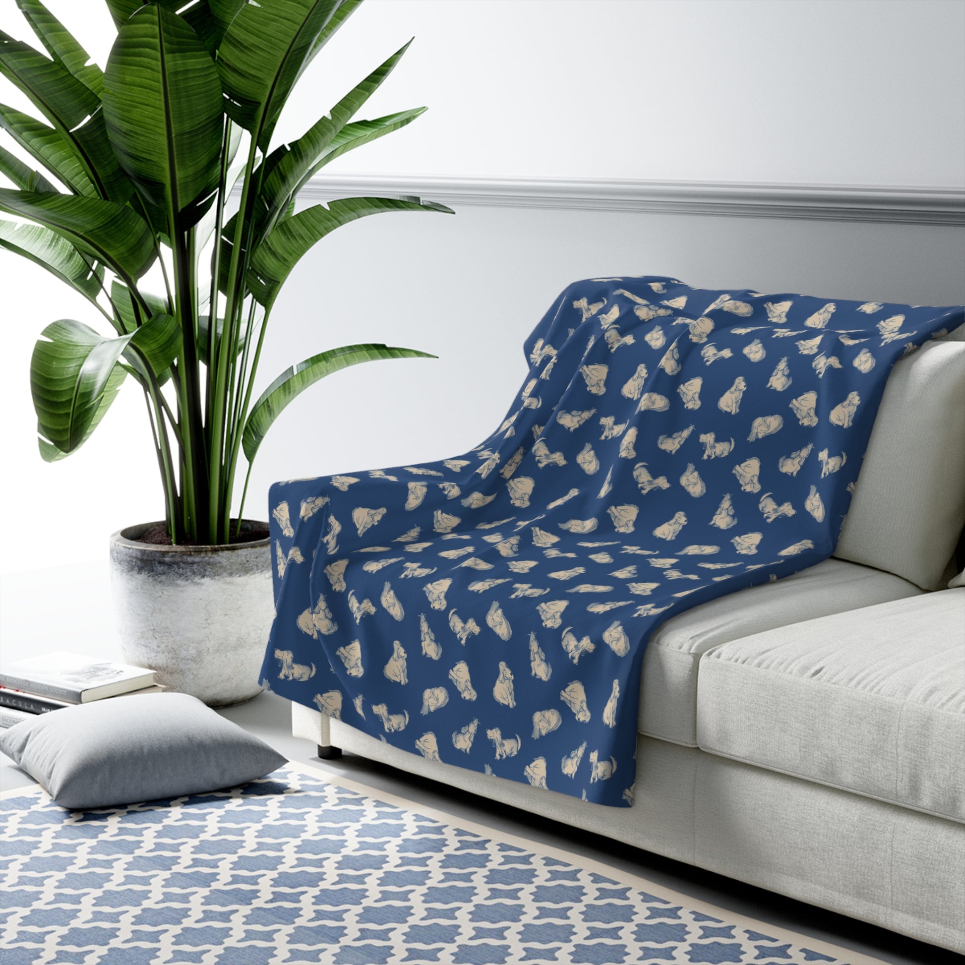 Blue patterned blanket draped over a white sofa in a living room with a plant and rug.