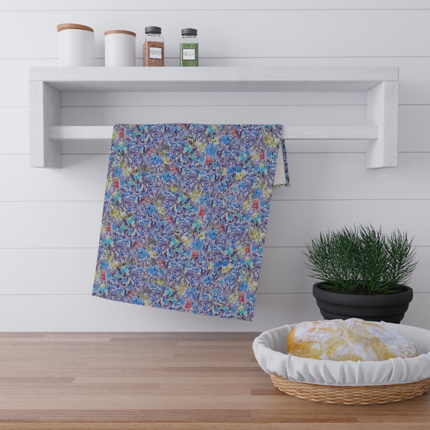 Colorful cool blues floral towel hanging on a white shelf with a plant and basket in the foreground.