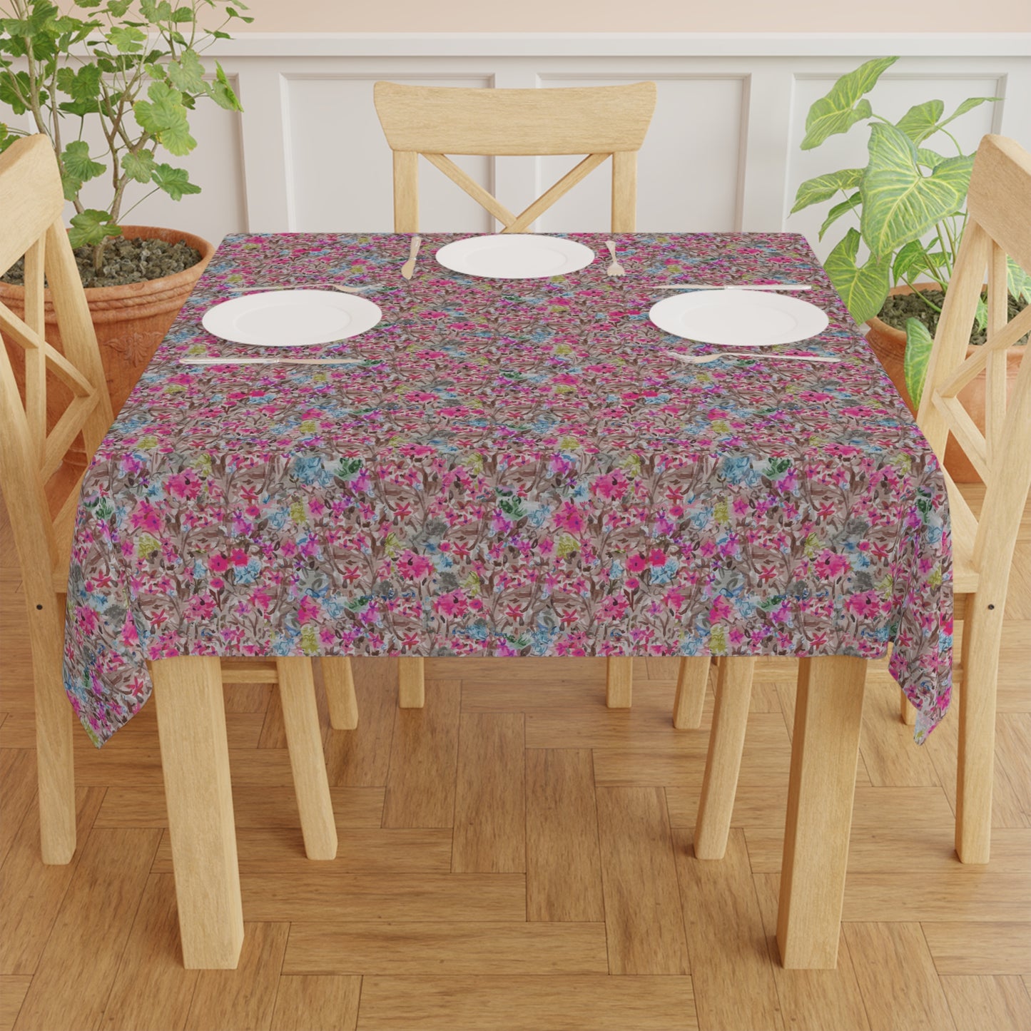 Table set with a floral tablecloth on a wooden table and chairs. Watercolor floral table cover with blooming branches in pink, blue, and neutral tones
