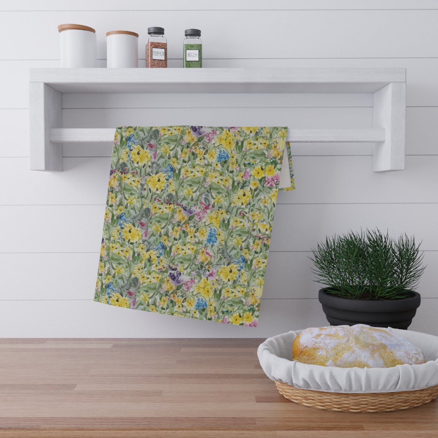 Watercolor wildflower tea towel featuring yellow, blue, and pink floral meadow pattern hanging on wooden kitchen rack.