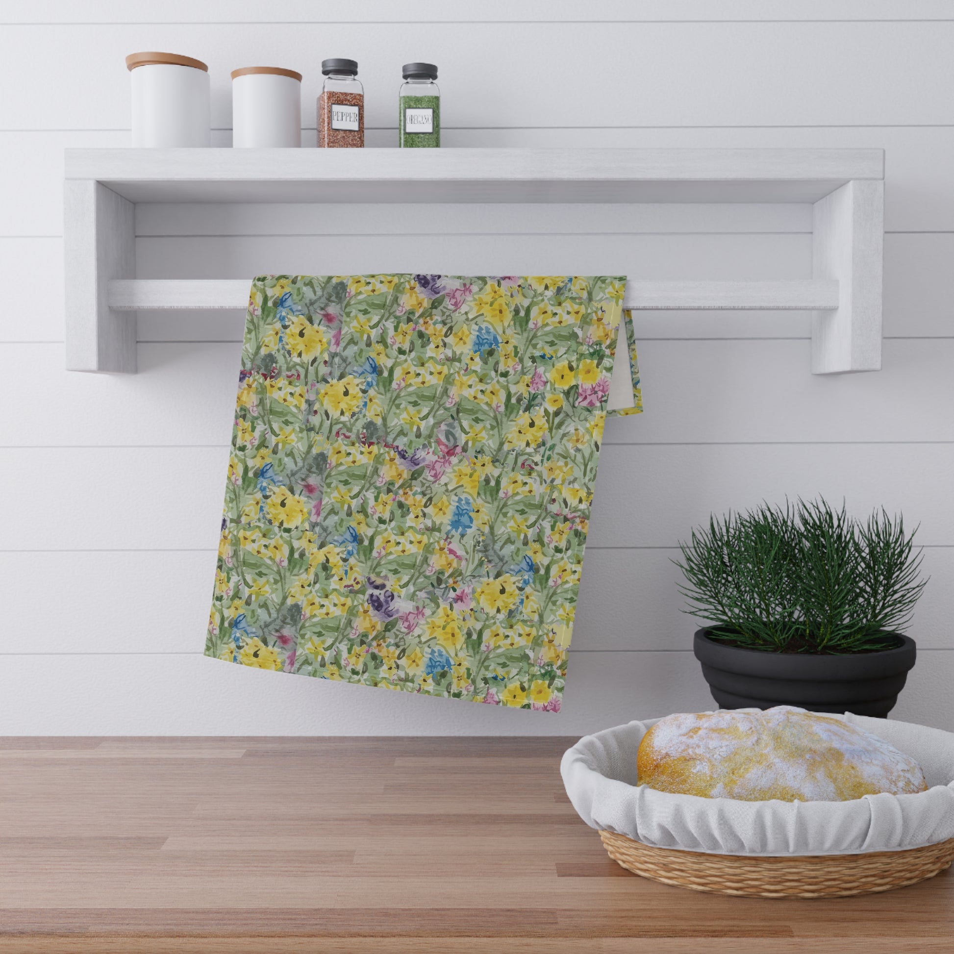 Watercolor wildflower tea towel featuring yellow, blue, and pink floral meadow pattern hanging on wooden kitchen rack.