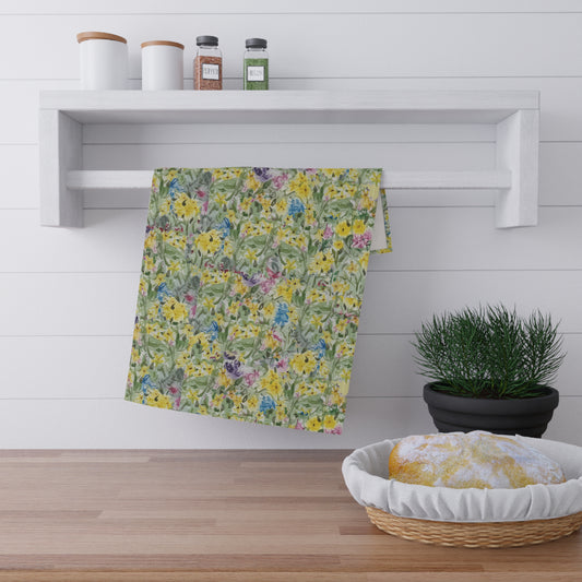 Watercolor wildflower tea towel featuring yellow, blue, and pink floral meadow pattern hanging on wooden kitchen rack.
