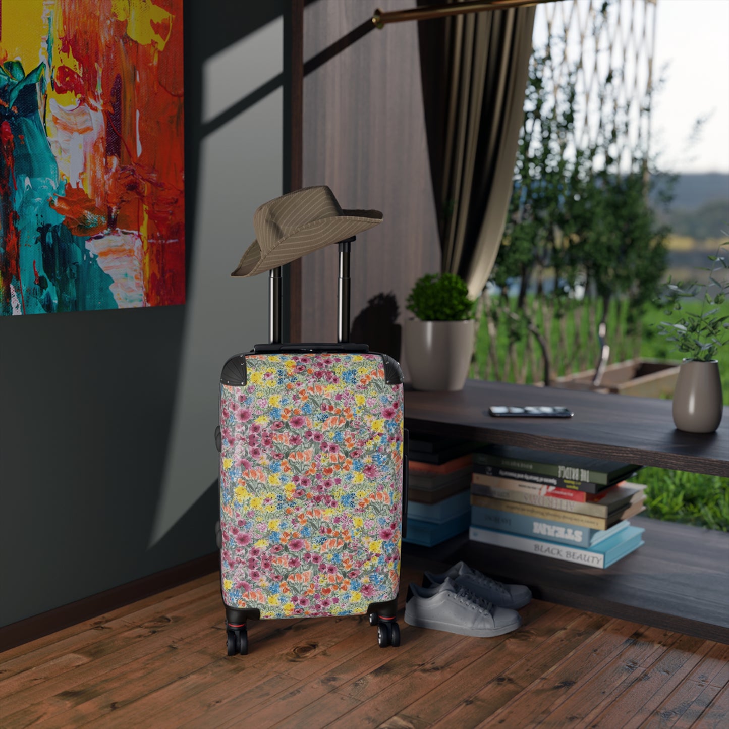 Floral-patterned suitcase with a hat on top in a room with books and a painting.