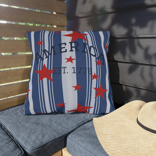 Decorative pillow with red stars and 'AMERICA EST. 1776' text on a wooden bench.