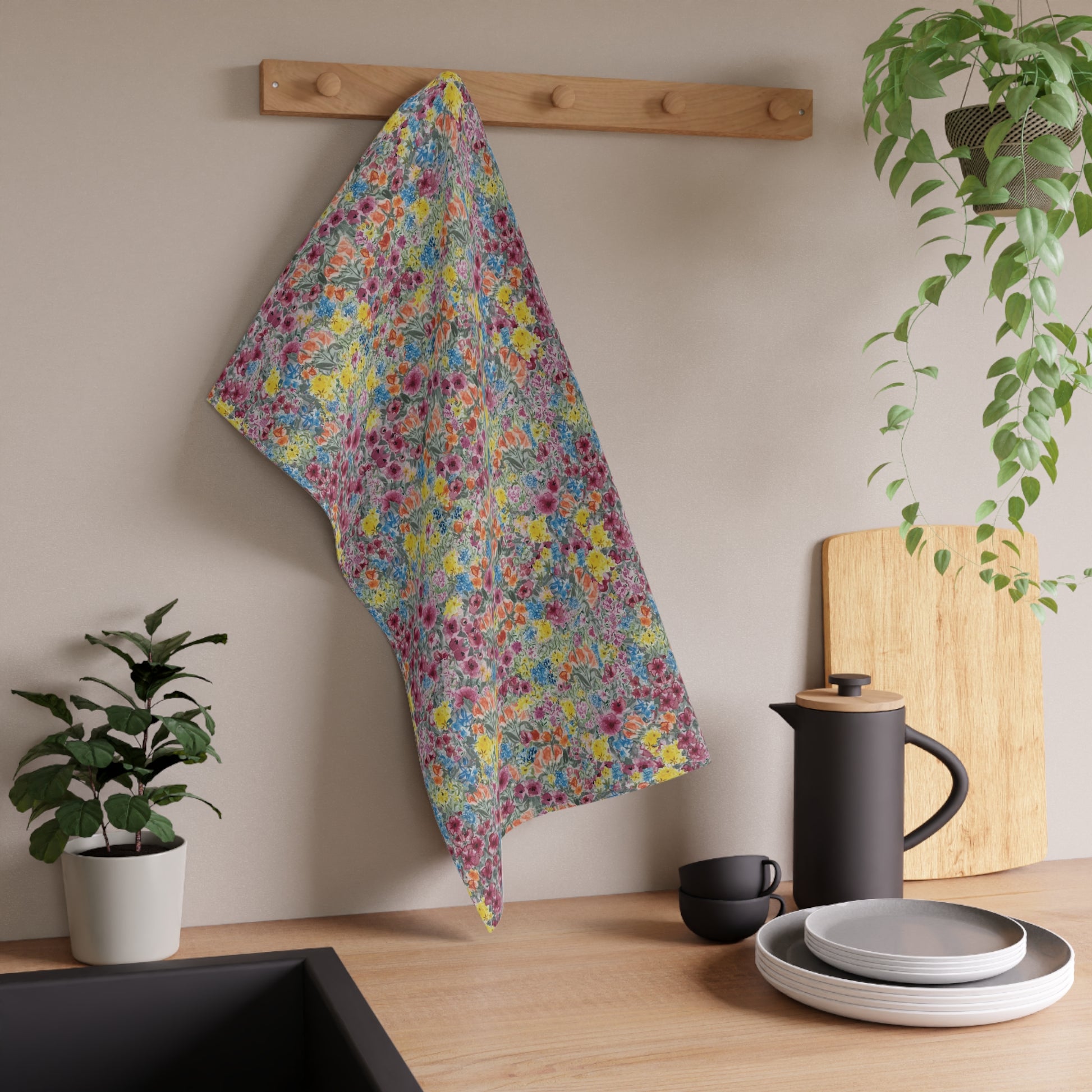 Floral towel hanging on a wooden rack above a kitchen counter with plates, cups, and a plant.
