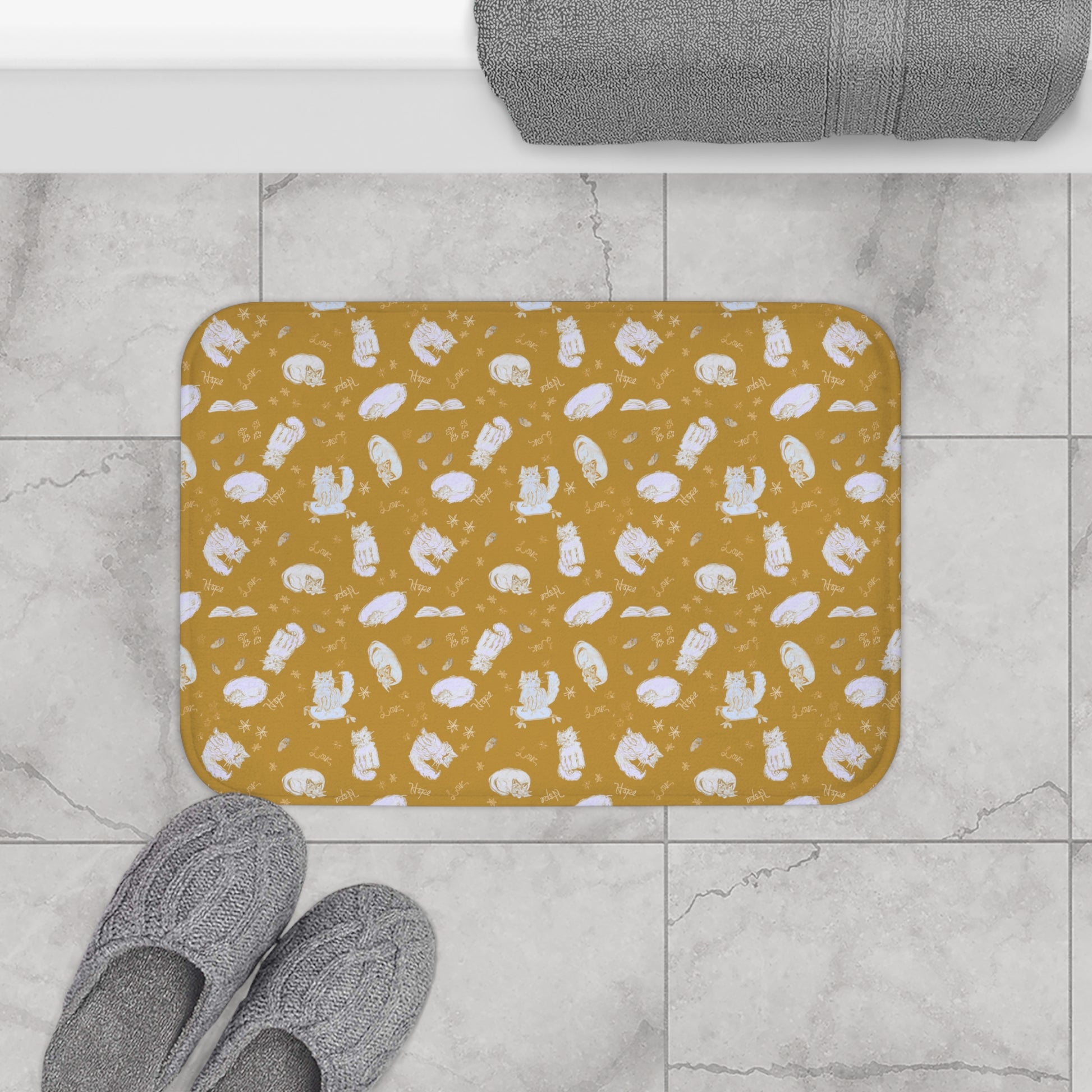 Mustard yellow bath mat featuring a cozy repeating pattern of sleeping and fluffy cats, books, stars, leaves, and handwritten words on a warm golden background, perfect for cat lovers and cozy home décor.