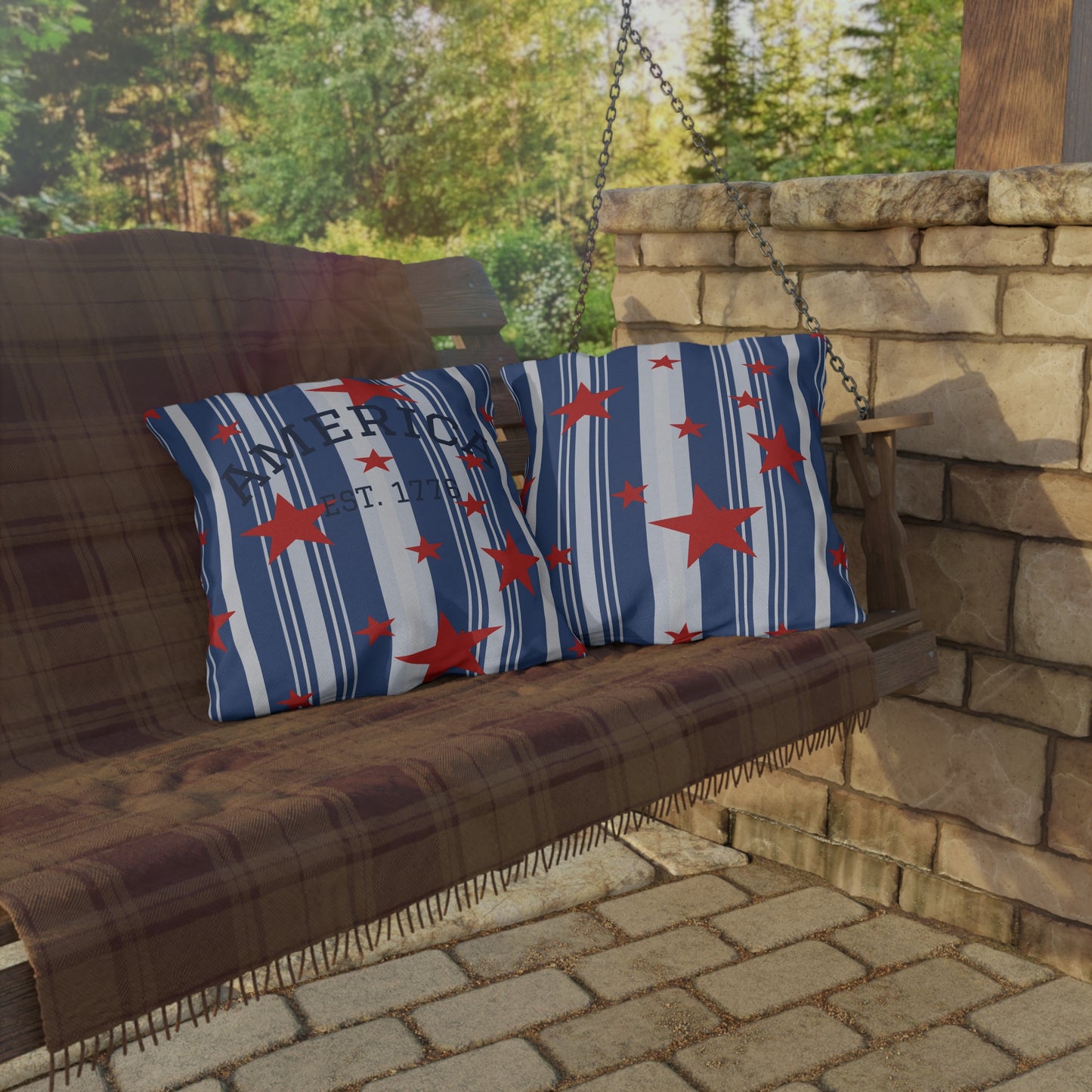 Brown wooden porch swing with blue pillows featuring red stars and white stripes, set against a stone wall and greenery.