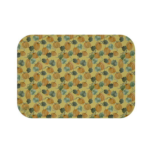 Memory foam bath mat with hand-painted pumpkins and curling vines in muted orange and sage on warm gold