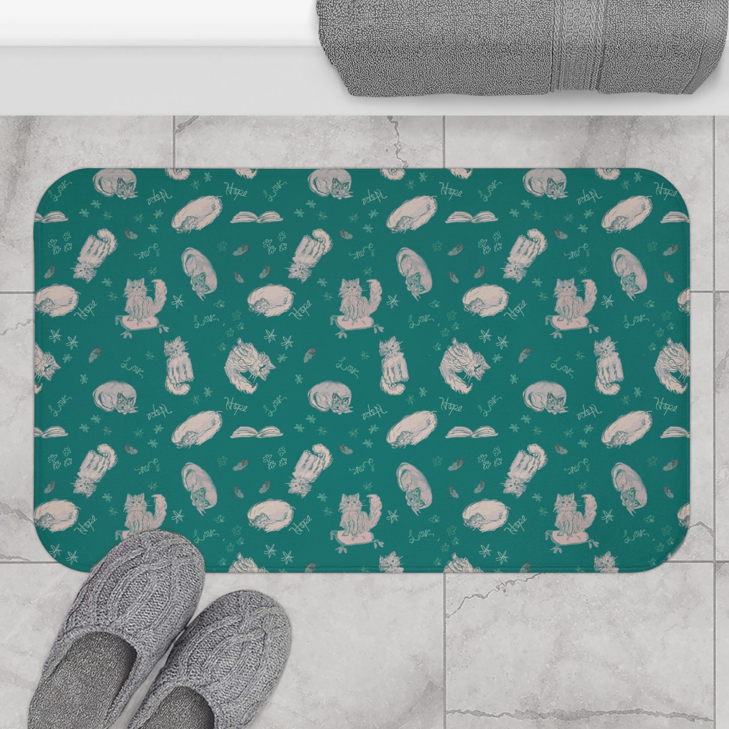 Teal bath mat with white cat pattern on a tiled floor with slippers.