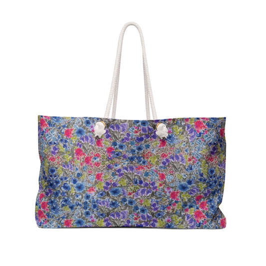 Blue and pink watercolor wildflower weekender bag with a vibrant meadow floral pattern and white rope handles, designed as a spacious travel tote for beach trips and weekend getaways.