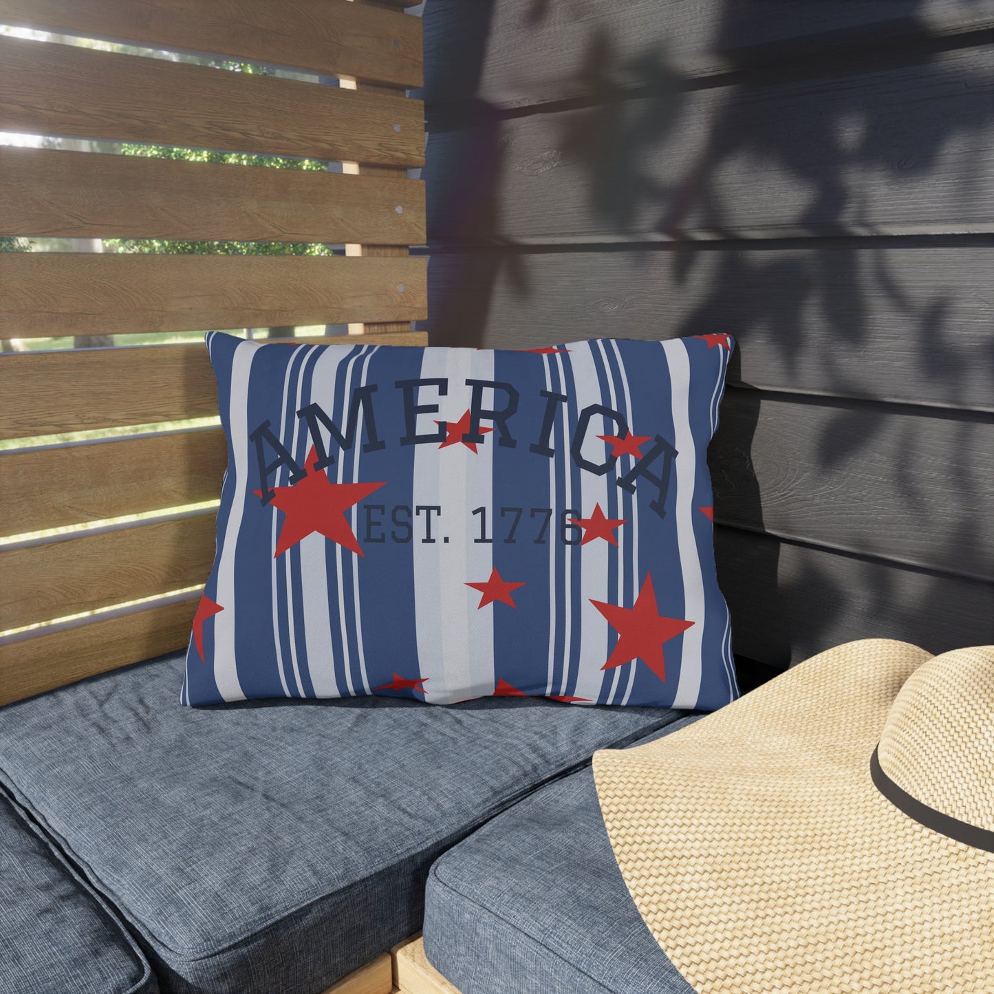 Pillow with 'America Est. 1776' text and red stars on a gray outdoor bench.