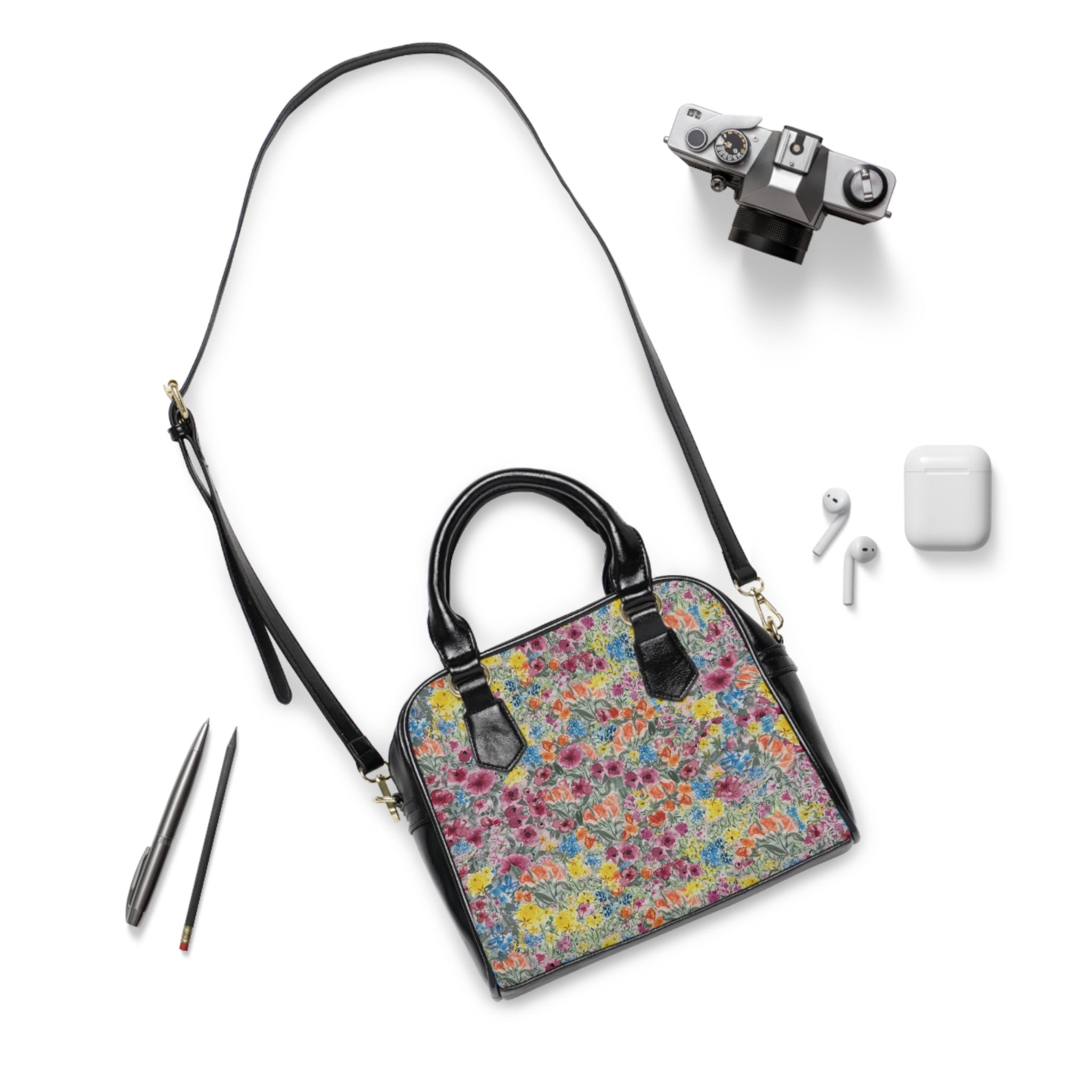 Floral patterned handbag with camera, earbuds, and pens on a white background