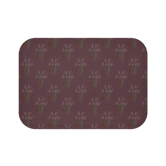 A rectangular bath mat with rounded corners. The mat features a repeating pattern of lavender-colored floral bouquets and small orange butterflies on a dark burgundy background. The mat is designed for bathroom use.