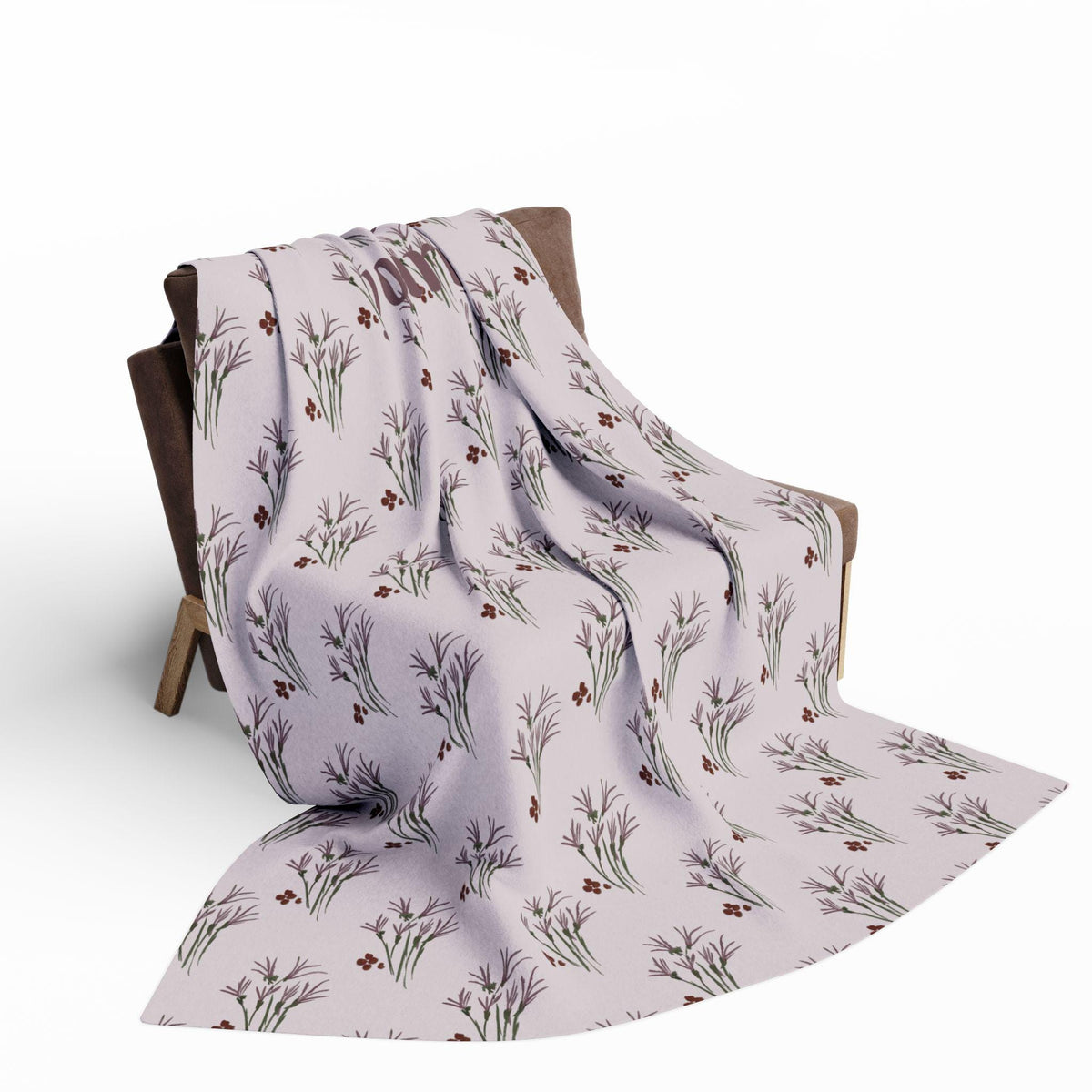 A light purple throw blanket draped over a wooden chair. The blanket features a repeating pattern of stylized floral sprigs in shades of green, brown, and red. The chair has a dark brown seat and back.