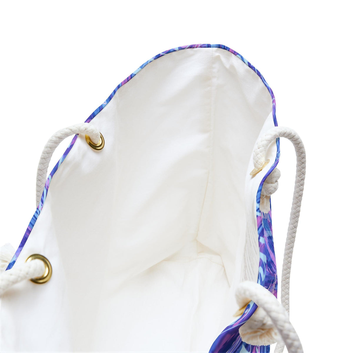 A white tote bag with a colorful abstract pattern in shades of blue, purple, and white. The bag has white rope handles and gold-colored grommets. The interior of the bag is white.