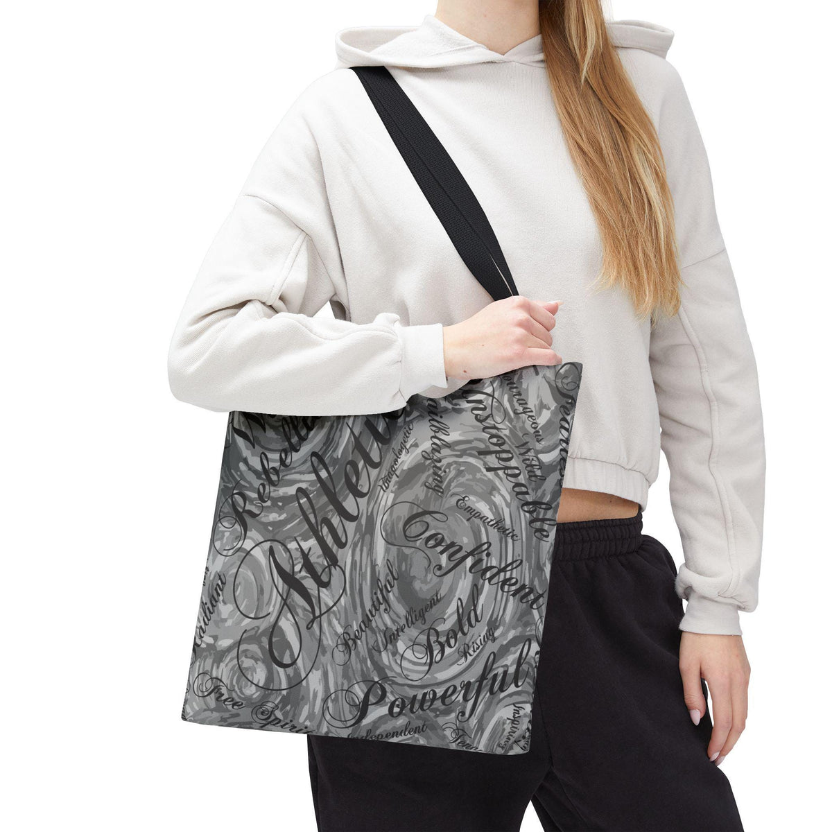 A gray tote bag with a black shoulder strap. The bag features a swirling, marbled design with motivational words like "Athlete," "Confident," and "Powerful" in a stylish font. The bag is carried over the shoulder.