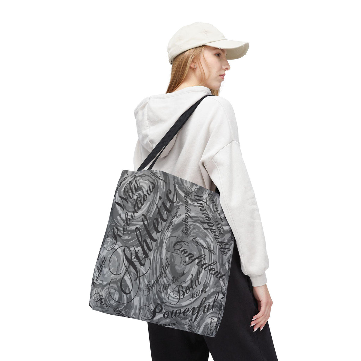 A gray and white tote bag with a swirling pattern and the word "Athletic" in large, black script. Other words like "Confident" and "Powerful" are also visible. The bag has black straps.