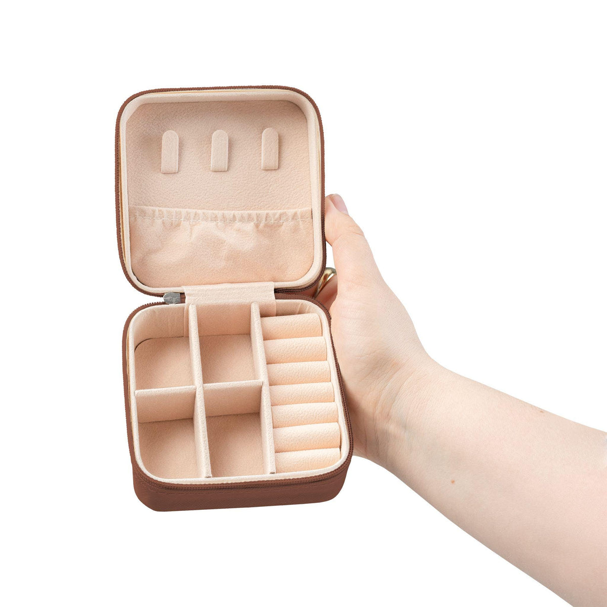 Open brown jewelry travel case with a beige interior. The case is square with a zipper closure and features compartments for rings, earrings, and other jewelry items. The case is held open by a hand.