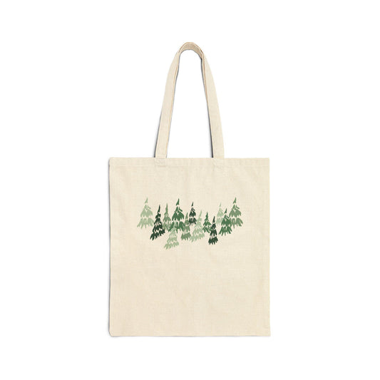 A cream-colored tote bag featuring a forest design in shades of green. The illustration depicts a cluster of stylized evergreen trees. The bag has two handles and is made of a sturdy fabric.