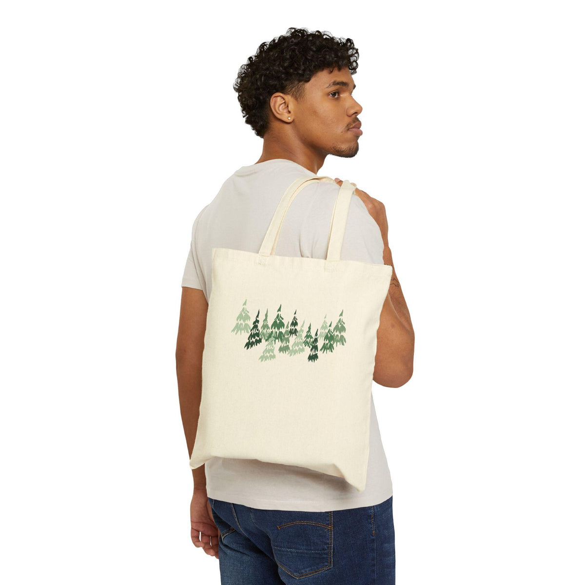 Cream-colored tote bag with a forest design. The bag features a repeating pattern of green and dark green pine trees. The bag has two cream-colored straps and is carried over the shoulder.