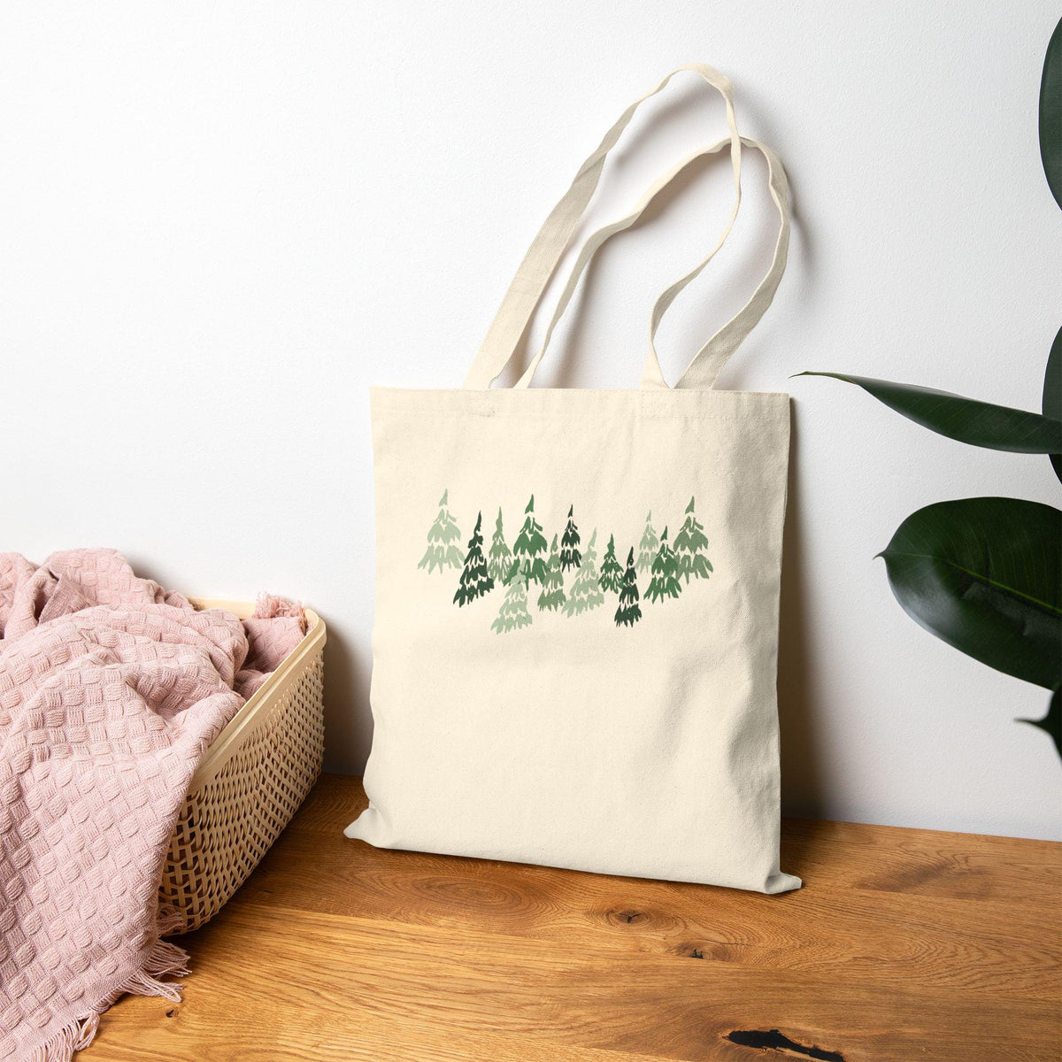 Cream-colored tote bag featuring a forest of stylized green trees. The trees vary in shades of green, creating a layered effect. The bag has long handles for carrying and is made of a sturdy fabric, perfect for shopping or carrying everyday items.