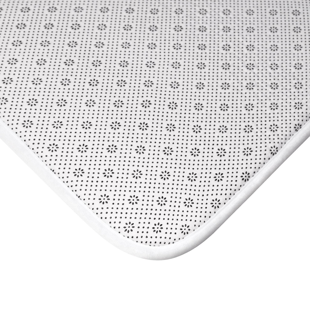 Close-up of a white-edged mat with a black and white floral pattern. The mat's surface is covered in small, evenly spaced black dots and floral designs, creating a textured appearance. The white edge provides a clean border.