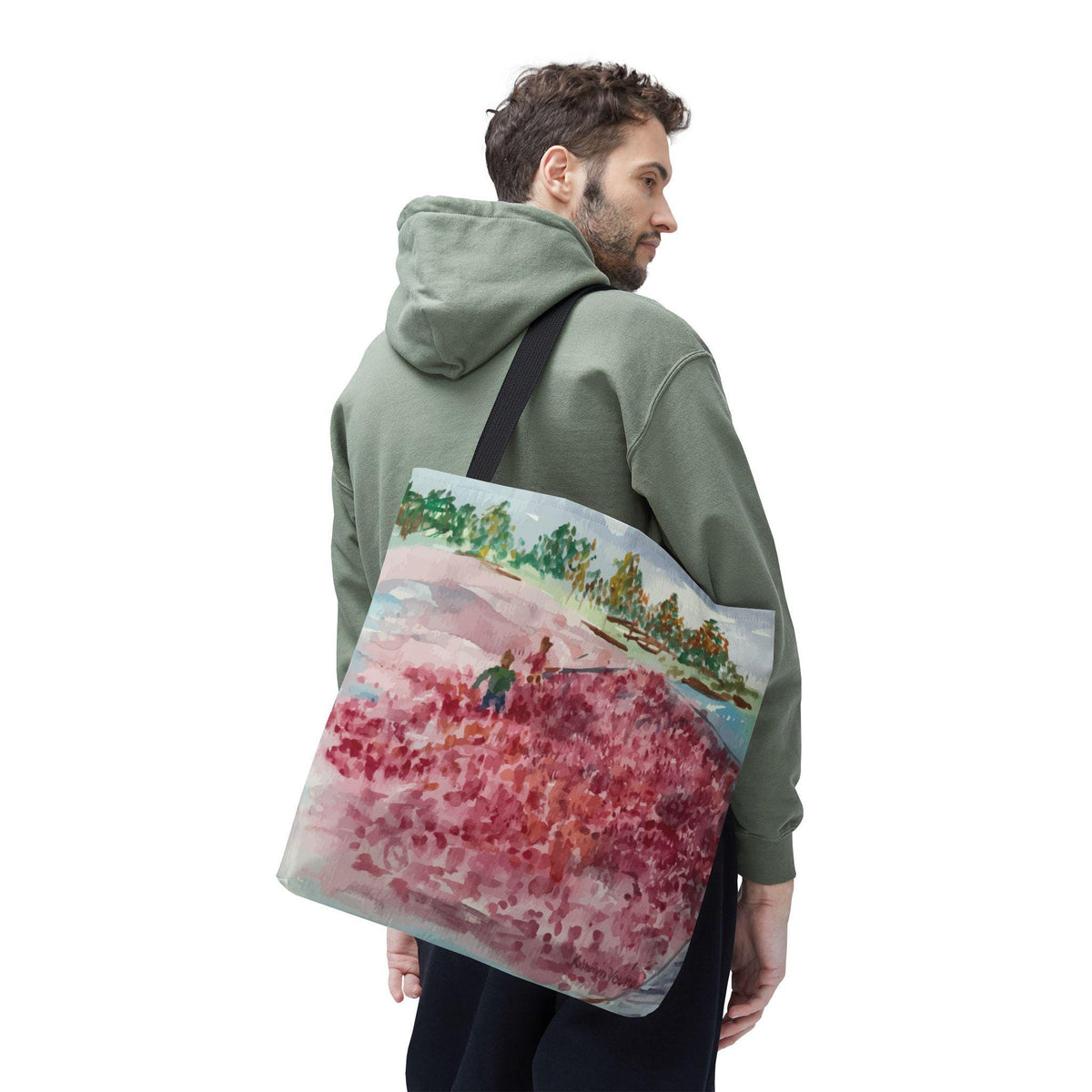 A canvas tote bag featuring a watercolor painting of a landscape with red and pink flowers, green trees, and a blue sky. The bag has a black shoulder strap and is carried over the shoulder.