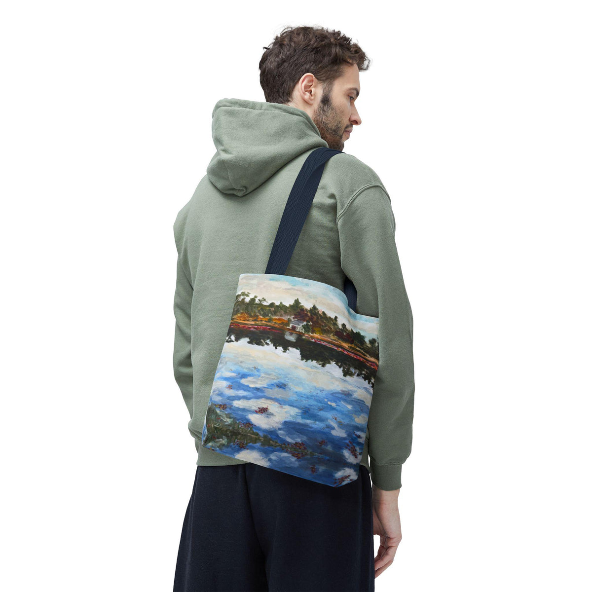 A canvas tote bag with a dark blue strap featuring a colorful impressionist painting of a lake scene. The artwork depicts a reflective body of water with trees and clouds. The bag is carried over the shoulder.