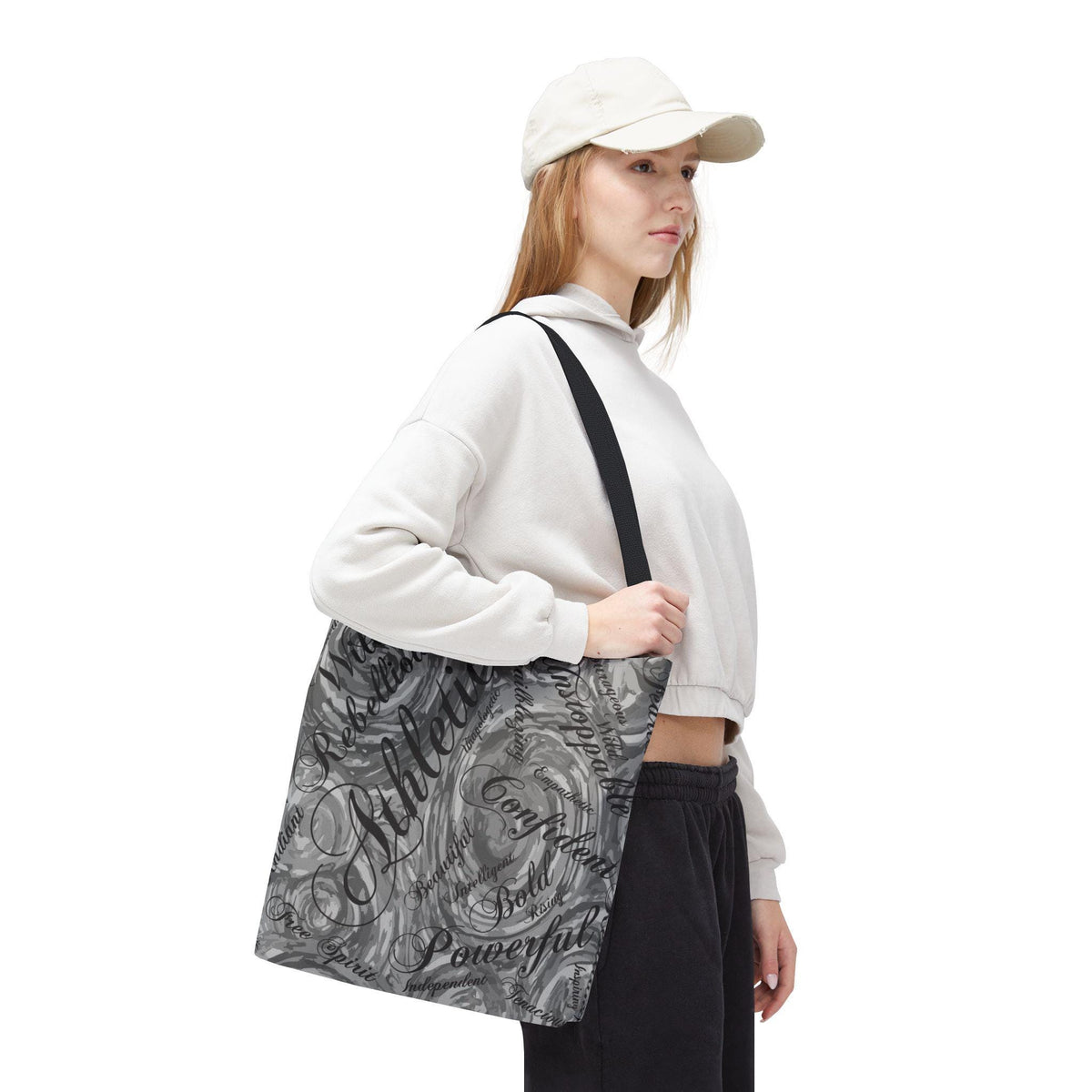 A gray and white tote bag with a black shoulder strap. The bag features a swirling design with motivational words like "Athlete," "Confident," and "Powerful" in a stylish font.