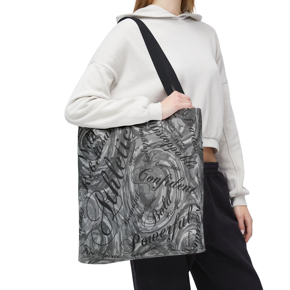 A gray and white tote bag with a black shoulder strap. The bag features a swirling design with motivational words like "Athletic," "Confident," and "Powerful" in a mix of fonts.