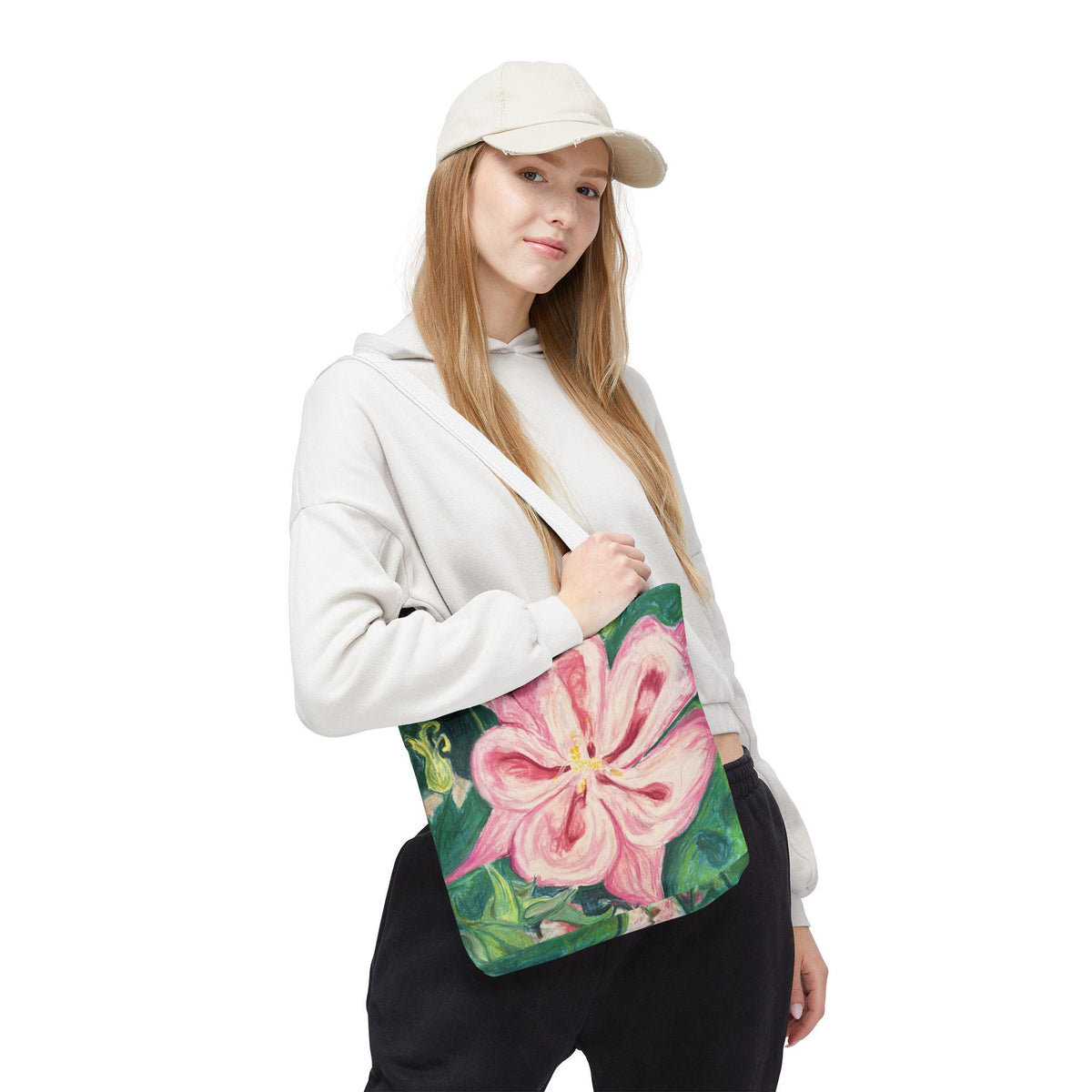 May include: A tote bag featuring a large, pink flower design with green foliage. The bag has a white strap and is held over the shoulder. The flower has a yellow center and is set against a dark green background .nature lover gift for her