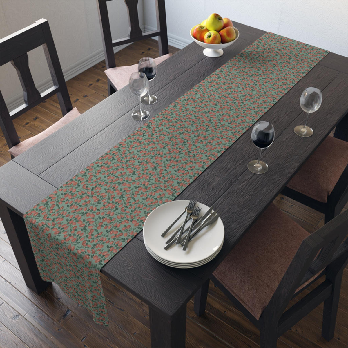 A long rectangular table runner featuring a repeating pattern of small red berries and green leaves on a muted sage green background, laid across a dark wooden dining table with white plates, silverware, and wine glasses.